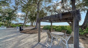 A beachside gazebo with a table and chairs, surrounded by trees and a view of the ocean. - Little Gull  2BR Cottage with Ultimate Views of the Famous Sunsets (Longboat Key)