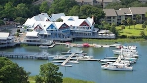 Un port de plaisance où sont amarrés plusieurs bateaux, un grand bâtiment à étages avec un toit particulier, et un pont qui relie le port à la zone des quais.