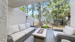 Un balcon doté de meubles en osier, d’un foyer et offrant une vue sur des arbres et une plage.