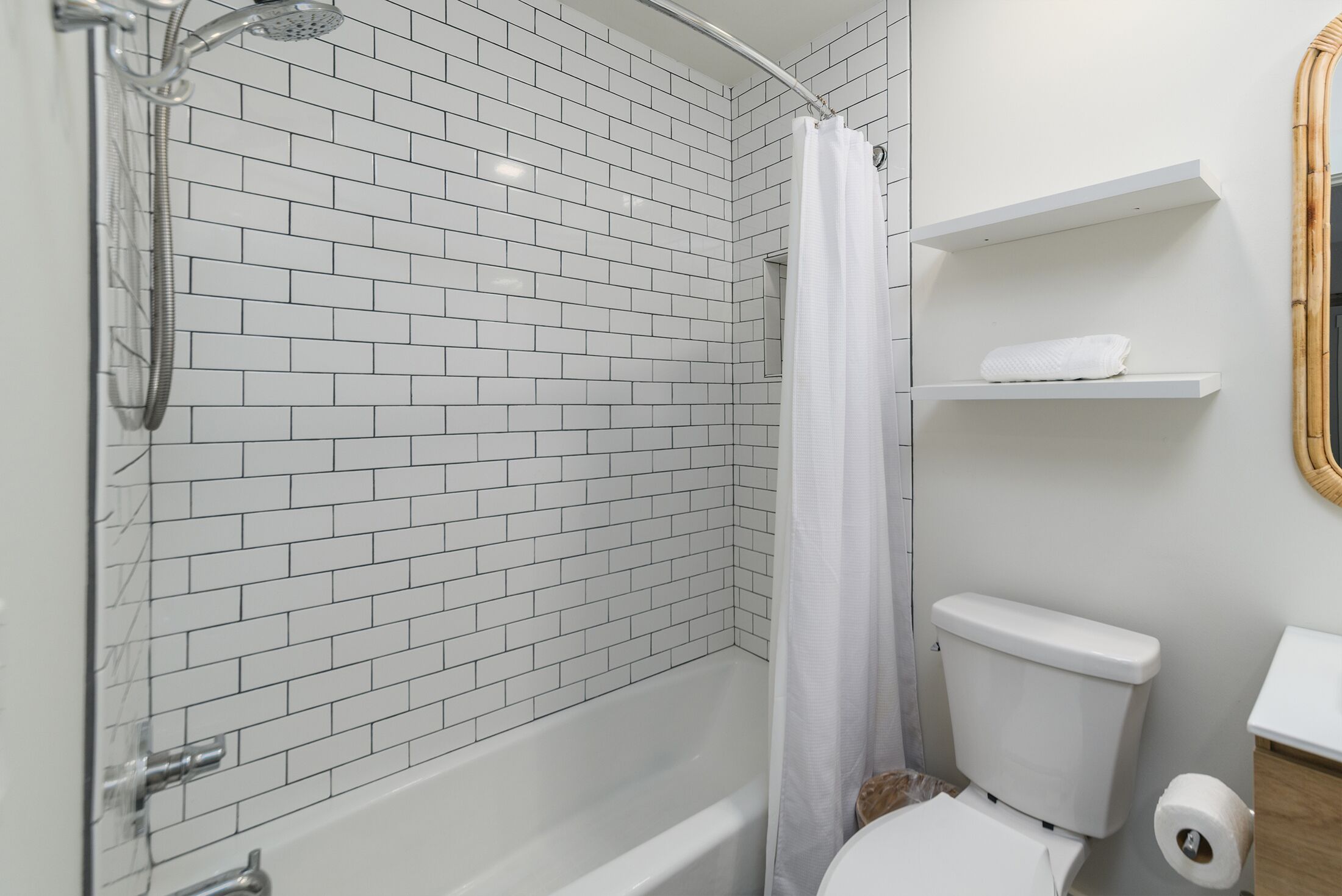 A bathroom with white subway tiles, a white bathtub, a toilet, and a shower curtain.