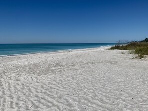Une vaste plage de sable fin, avec une eau d’un bleu limpide et un ciel dégagé.