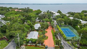An aerial view of a residential area with a tennis court, houses, and a road leading to the water. - Throwback Charm Meets Beach Bliss 1BR Cottage (Longboat Key)