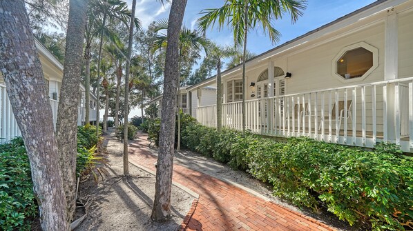 A pathway flanked by trees and a white building with a balcony.