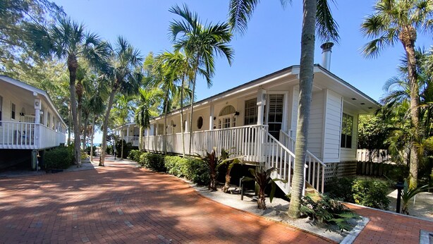 A two-story house with a covered porch, surrounded by palm trees and a brick pathway. - 1BR Gulf Breezes & Old Florida Charm (Longboat Key)