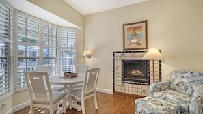 A dining area with a table and chairs, a fireplace with a tiled surround, and a sofa with a patterned cover.