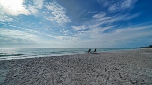 A beach with two empty lounge chairs facing the ocean, under a partly cloudy sky. - Gulf-Front Charm with Old Florida Soul-2BR Cottage (Longboat Key)
