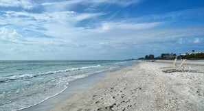 A beach with a clear sky, calm sea, and a row of empty beach chairs. - 2BR Cottage Bayside of Property, Full Resort Amenities (Longboat Key)