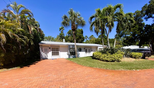 A single-story house with a brick driveway, surrounded by palm trees and a well-maintained lawn. - 2BR Cottage Bayside of Property, Full Resort Amenities (Longboat Key)