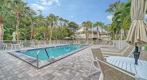 A rectangular swimming pool with a tiled deck, surrounded by lounge chairs and umbrellas, with a building in the background. - 2BR Cottage Bayside Close to the Pool (Longboat Key)