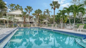 A swimming pool with lounge chairs and umbrellas, surrounded by palm trees and a building with a balcony. - 2BR Cottage Bayside Close to the Pool (Longboat Key)