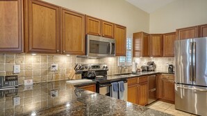 A kitchen with wooden cabinets, stainless steel appliances, a granite countertop, and a tiled backsplash. - 2BR Cottage Bayside Close to the Pool (Longboat Key)