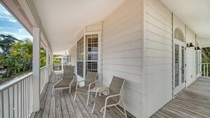A covered porch with white railings, wicker chairs, and a view of a road and greenery. - 2BR Cottage Bayside Close to the Pool (Longboat Key)