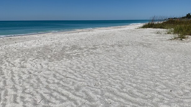 Una extensa playa de arena con aguas azules cristalinas y un cielo despejado.