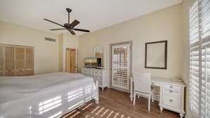 Un dormitorio con cama, escritorio, silla, televisión, ventilador de techo y armario.