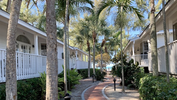 A pathway lined with palm trees and a brick walkway leading to a building with white railings and a covered porch. - 3BR Cottage- Footsteps to the Sand (Longboat Key)