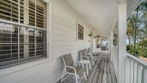 A covered porch with white railings, a wooden deck, and several wicker chairs. - 3BR Cottage- Footsteps to the Sand (Longboat Key)