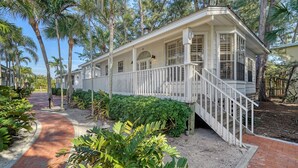 A white building with a covered porch and a staircase leading to a deck. - 3BR Cottage- Footsteps to the Sand (Longboat Key)