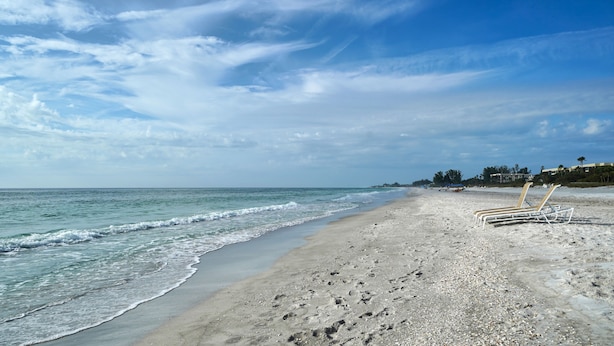 Een strand met een zandstrand, enkele ligstoelen en een heldere lucht.