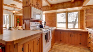 A wooden cabin kitchen with a large window, wooden cabinets, and a white stove. - 'Away at Moose Bay' Breezy Point Gem w/ Game Room (Breezy Point)