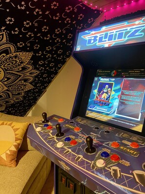 A gaming console with a screen displaying a football video game, surrounded by a decorative tapestry and a couch. - 4BR New England Style Home (Vermilion)