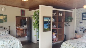Un dormitorio acogedor con dos camas, techo de madera, zona de cocina y una estantería.