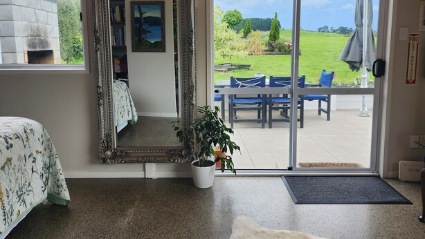 Habitación de hotel con un espejo grande, una cama con cubrecama floral, una planta en maceta y vistas al exterior a través de un ventanal.