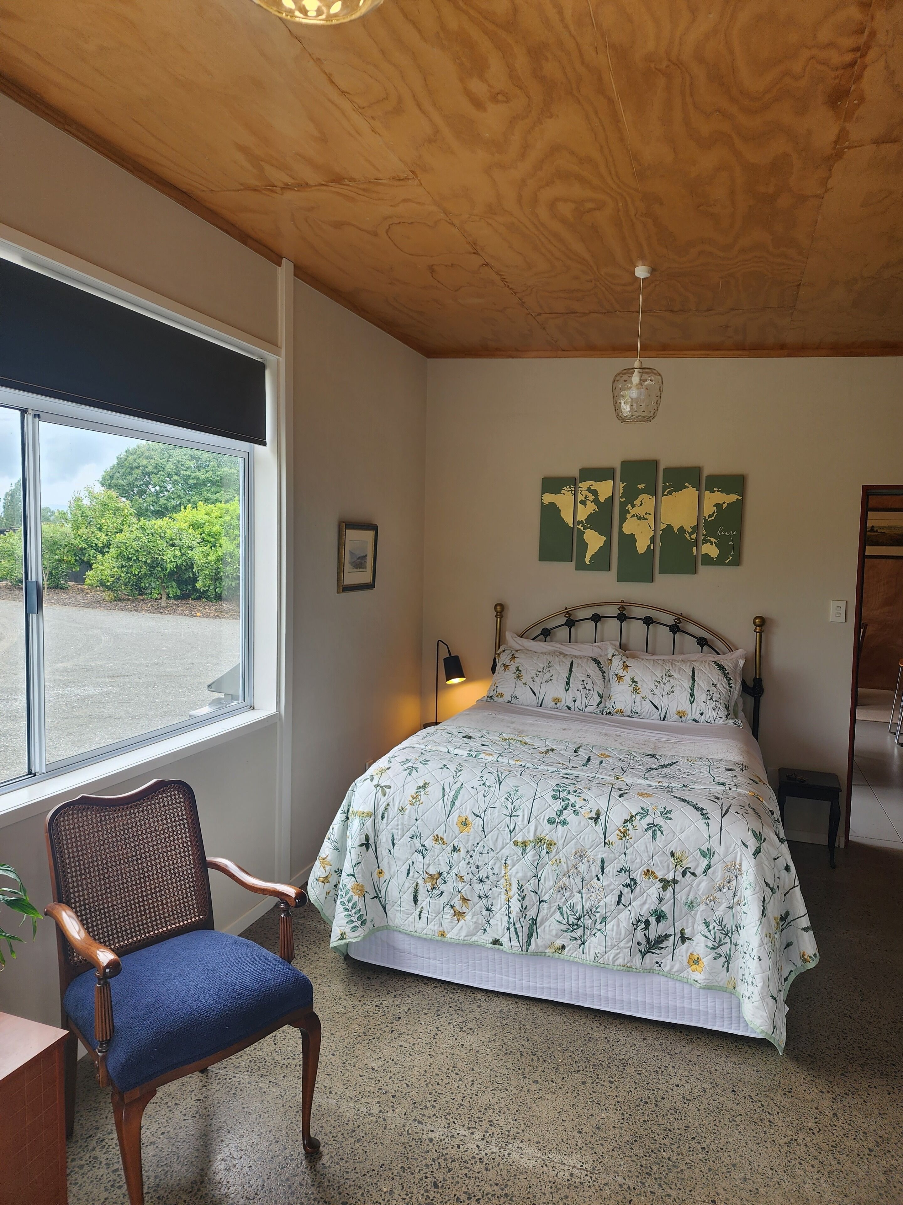 A bedroom with a bed, a chair, a window, a world map on the wall, and a ceiling light.