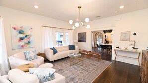 A modern living room with a white sofa, a coffee table, and a rug. There is a dining area in the background with a table and chairs.