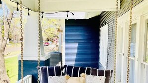 A porch swing with a white mattress and patterned pillows, supported by wooden posts and metal chains.