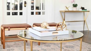 A modern room with a glass coffee table, two brown leather stools, a whiteboard, and a small plant on a side table.