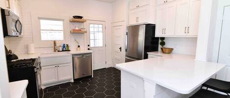 A modern kitchen with white cabinets, a black hexagonal floor, stainless steel appliances, and a central island.