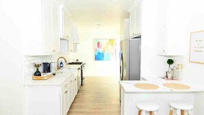 A modern kitchen with white cabinetry, a central island with stools, and a large window with a colorful painting. - A Modern luxury oasis on the plaza (Oklahoma City)
