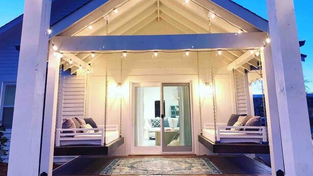 A covered porch with swing seats and string lights, leading to a glass door entrance. - A Modern luxury oasis on the plaza (Oklahoma City)