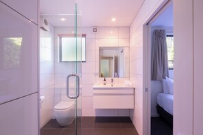 A modern bathroom with a glass shower enclosure, a toilet, a sink with a mirror, and a bed visible through an open door. - Prime Location | 3 bedroom home | Unlimited WIFI (Queenstown)
