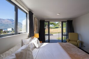 A hotel room with a large bed, a chair, a window with a view of mountains, and a balcony. - Prime Location | 3 bedroom home | Unlimited WIFI (Queenstown)