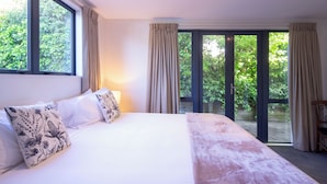 A bedroom with a large bed, a view of greenery through a sliding glass door, and a ceiling light. - Prime Location | 3 bedroom home | Unlimited WIFI (Queenstown)