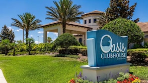 A sign for Oasis Clubhouse at ChampionsGate, surrounded by well-maintained lawns and various plants. - Luxury Champions Gate Condo, Resort-Style Retreat (Four Corners)