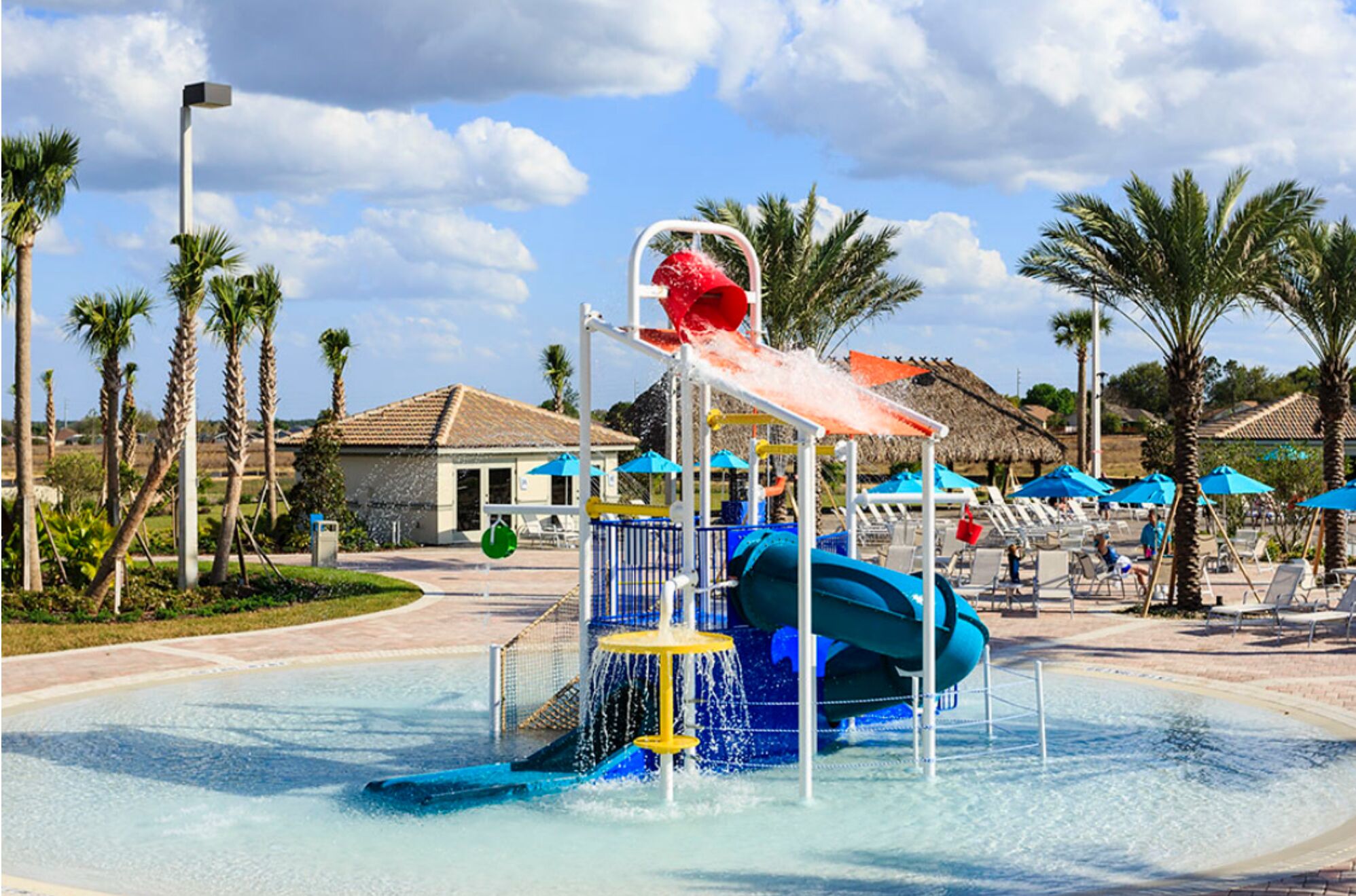 A water park with a blue water slide, a red water feature, and lounge chairs under blue umbrellas.