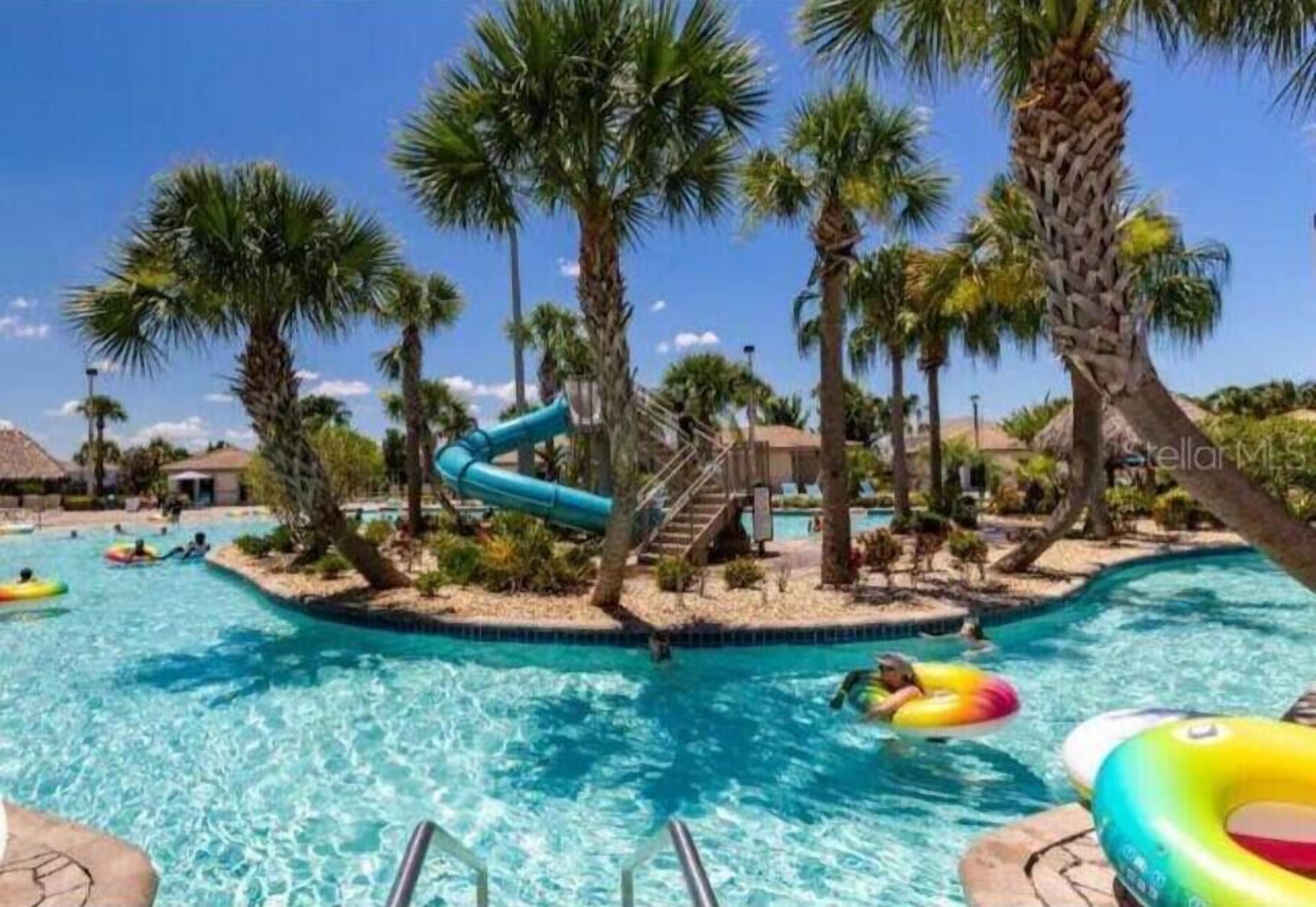 A swimming pool with palm trees, a slide, and inflatable rings.