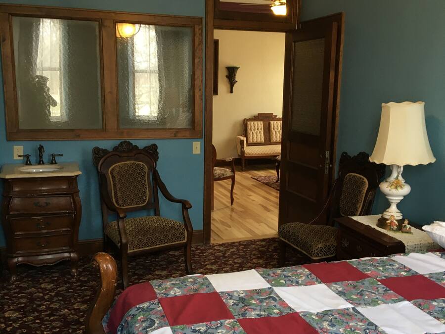 A bedroom with a wooden bed, a dresser, a mirror, a chair, and a lamp.