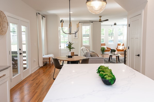 A modern kitchen with a marble island, wooden flooring, and a dining area with a round table and chairs.