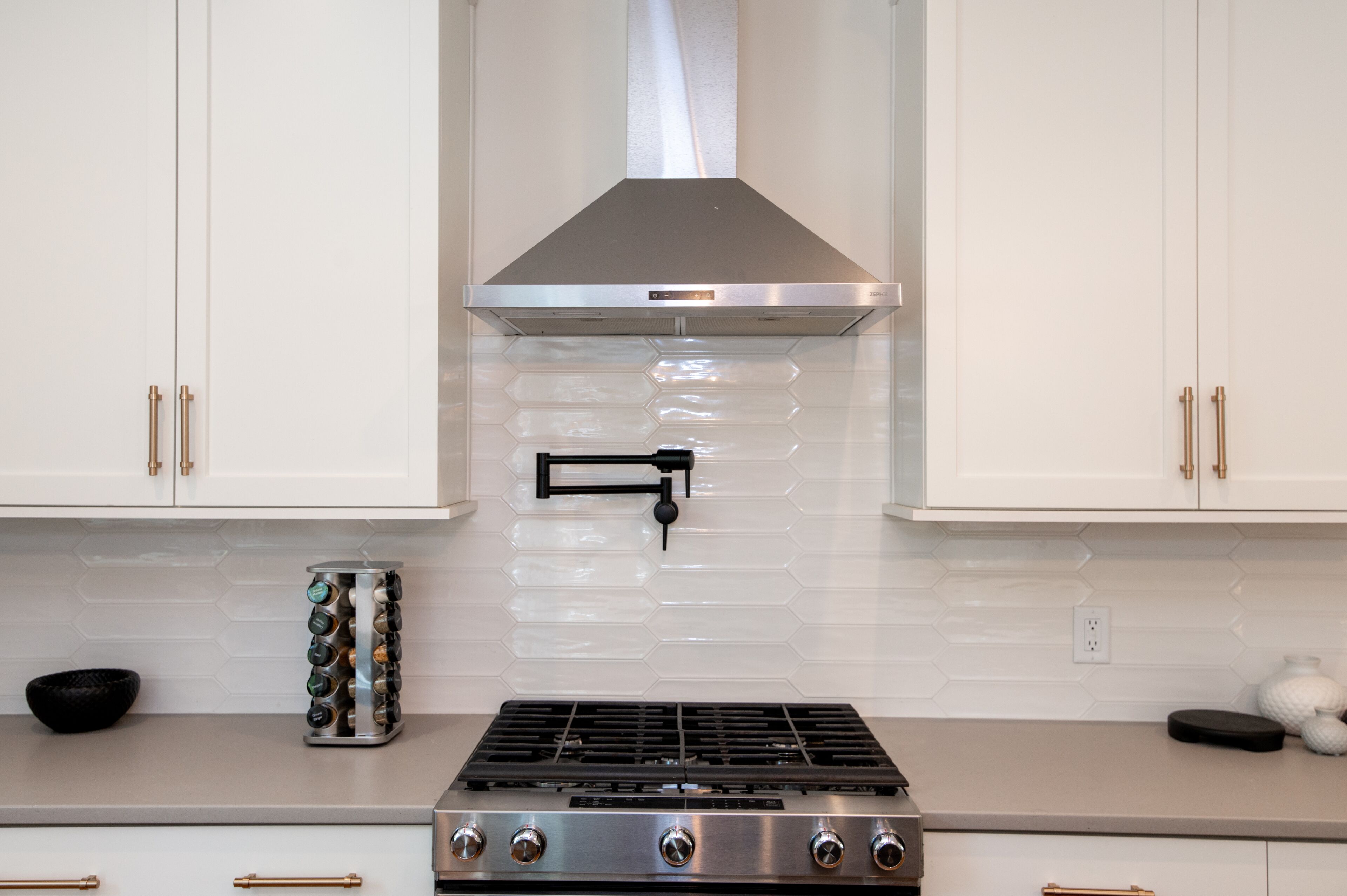 Una cocina con armarios blancos, una campana extractora de acero inoxidable, un salpicadero de azulejos hexagonales y una estufa a gas.
