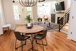 A modern living room with a wooden dining table, black chairs, a sofa, and a fireplace.