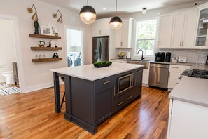 A modern kitchen with a central island, wooden shelves, and stainless steel appliances.