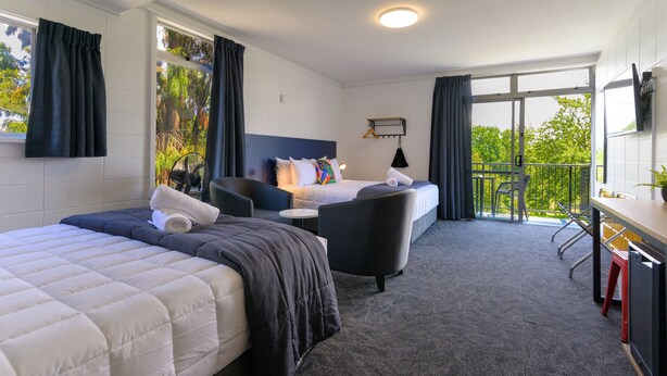 A hotel room with two beds, a desk, a chair, and a balcony with a view of trees. - Urban Lounge Sleepery, SureStay Collection by BW (Rotorua)