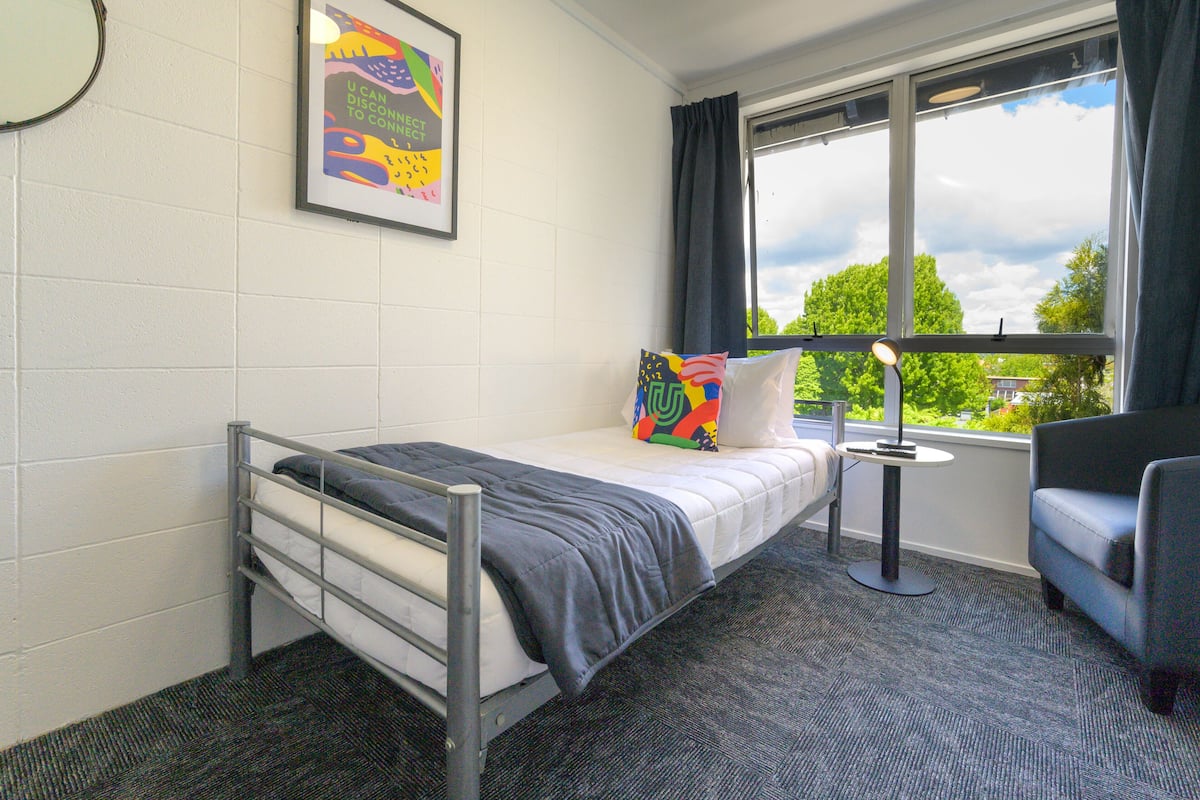 A small, single-bed room with a window, a desk, and a chair.