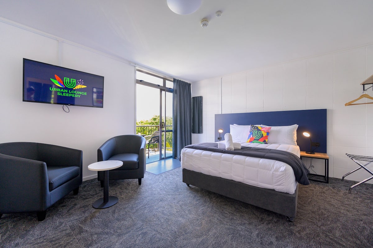 A hotel room with a bed, a sofa, a small table, a TV, and a view of the outdoors.