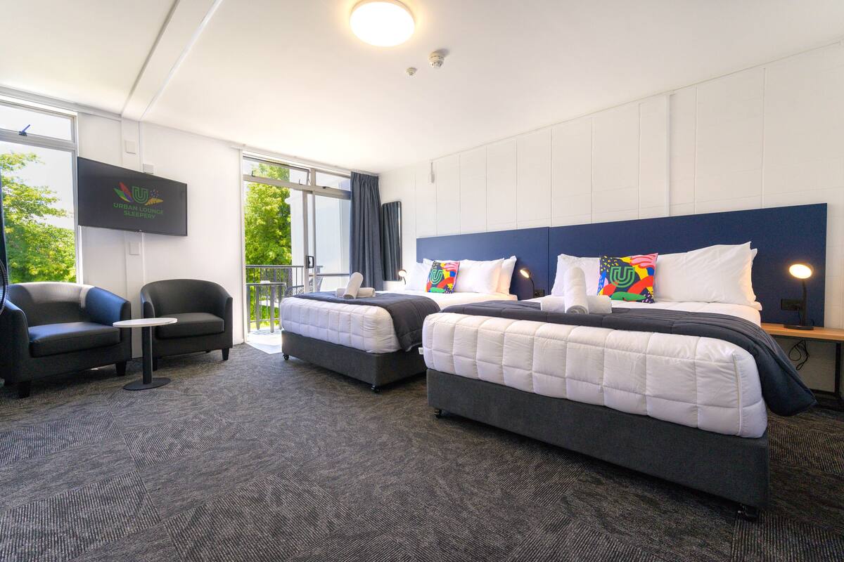 A hotel room with two beds, a TV, a small table, and a sofa.