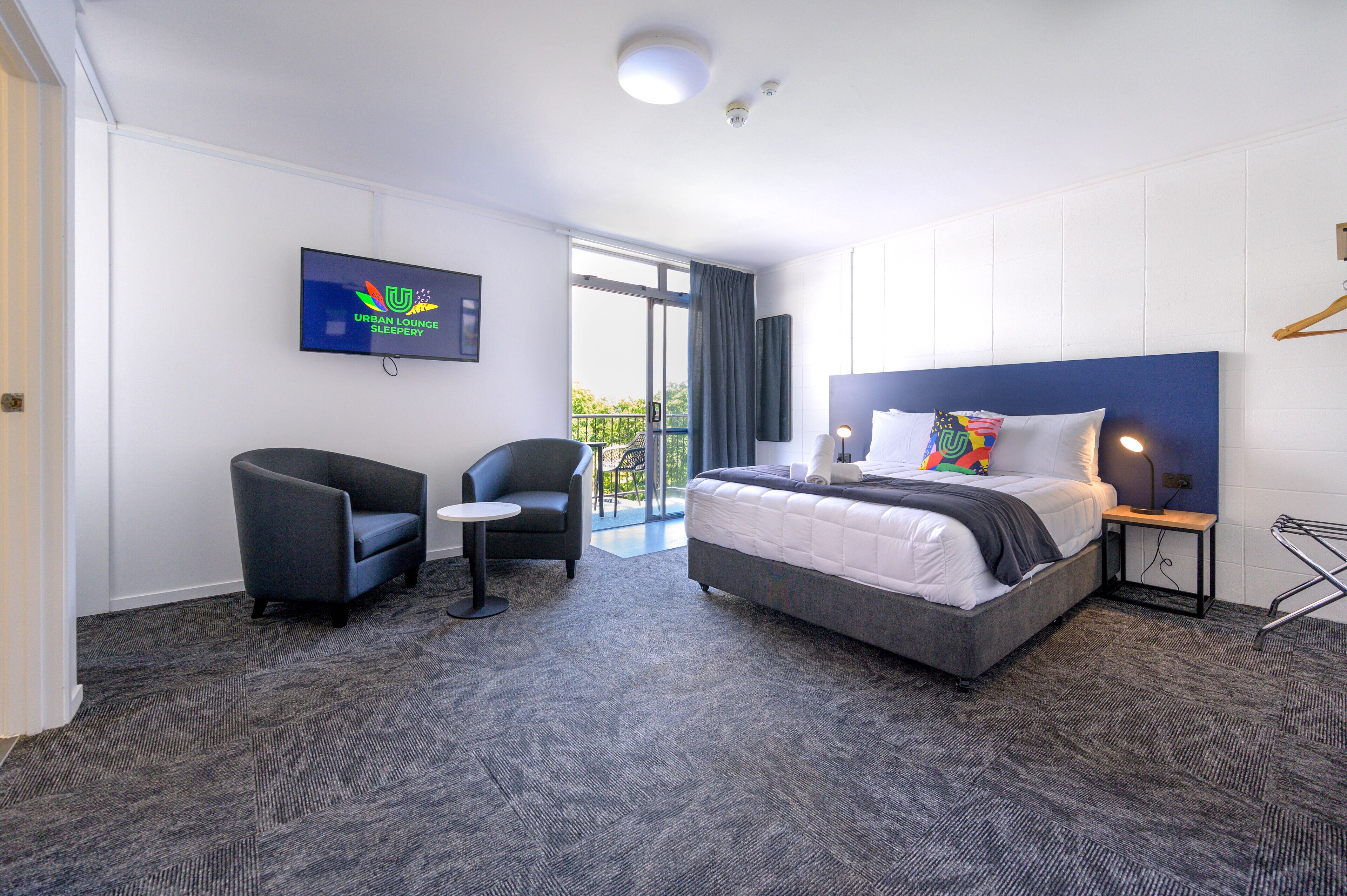 Quarto de hotel com cama, uma cadeira, televisão e vista para o exterior.