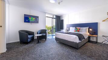 Quarto de hotel com cama, uma cadeira, televisão e vista para o exterior.